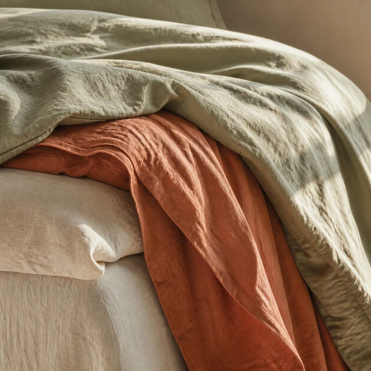 Layered sage green and terracotta linen bedding in morning light